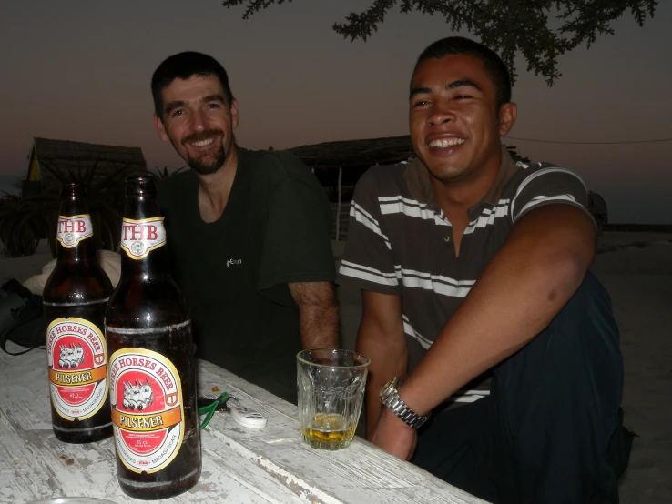 two men are sitting at a table with beers