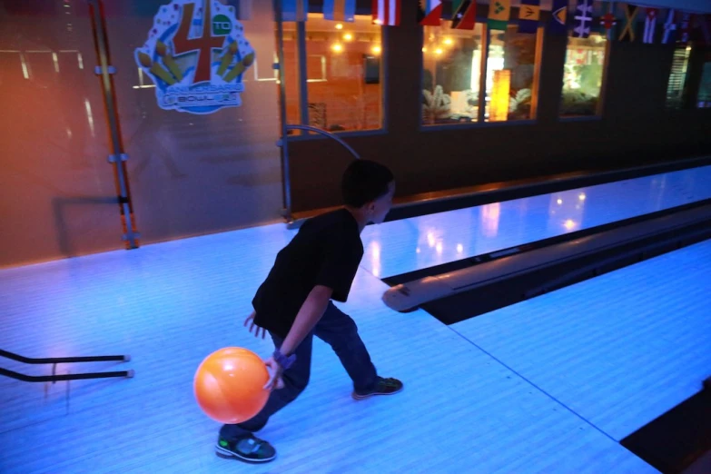 a little boy playing with an orange ball at a bowling alley