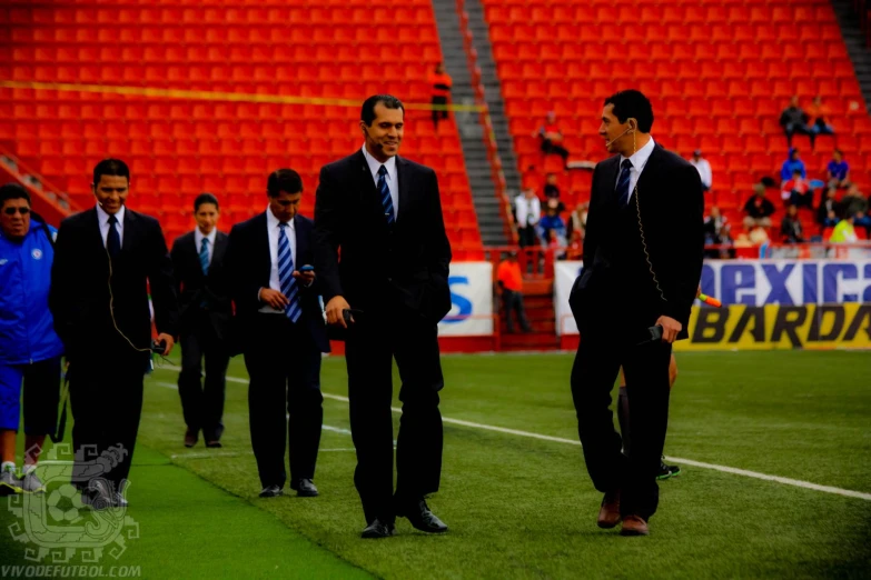 two men and one is wearing suit standing on the soccer field