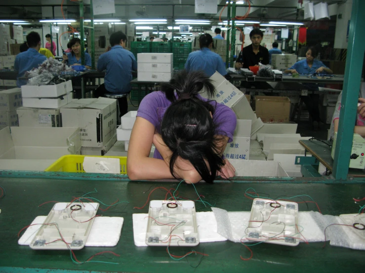 two women are sitting at an assembly line of some kind