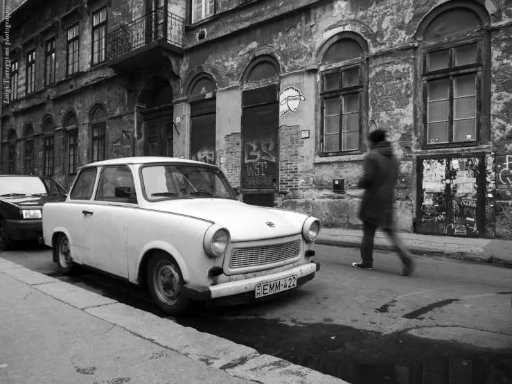 the man is walking by an old car on the side walk