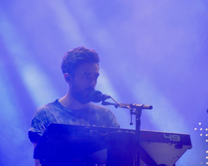 man sitting at keyboard singing into microphone on stage