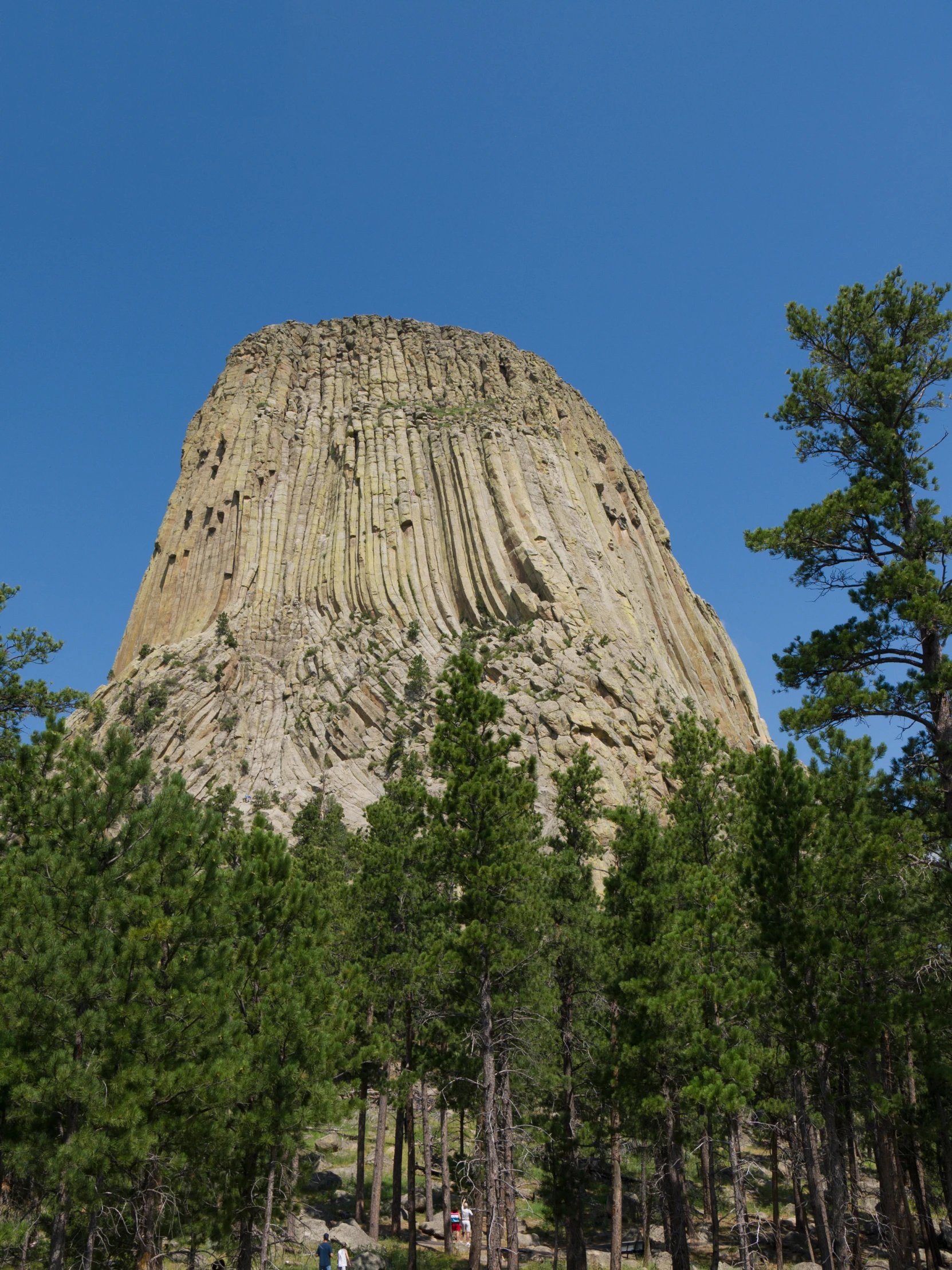 three people in the distance walking in front of a tall rocky mountain