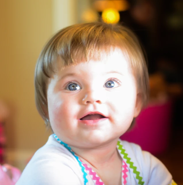 this toddler is wearing a rainbow necklace and smiling at the camera