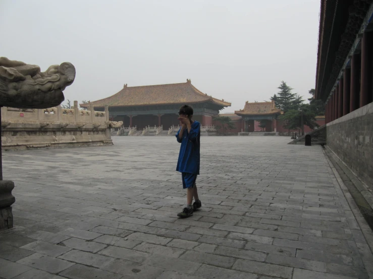 a boy talking on a phone walking across a courtyard