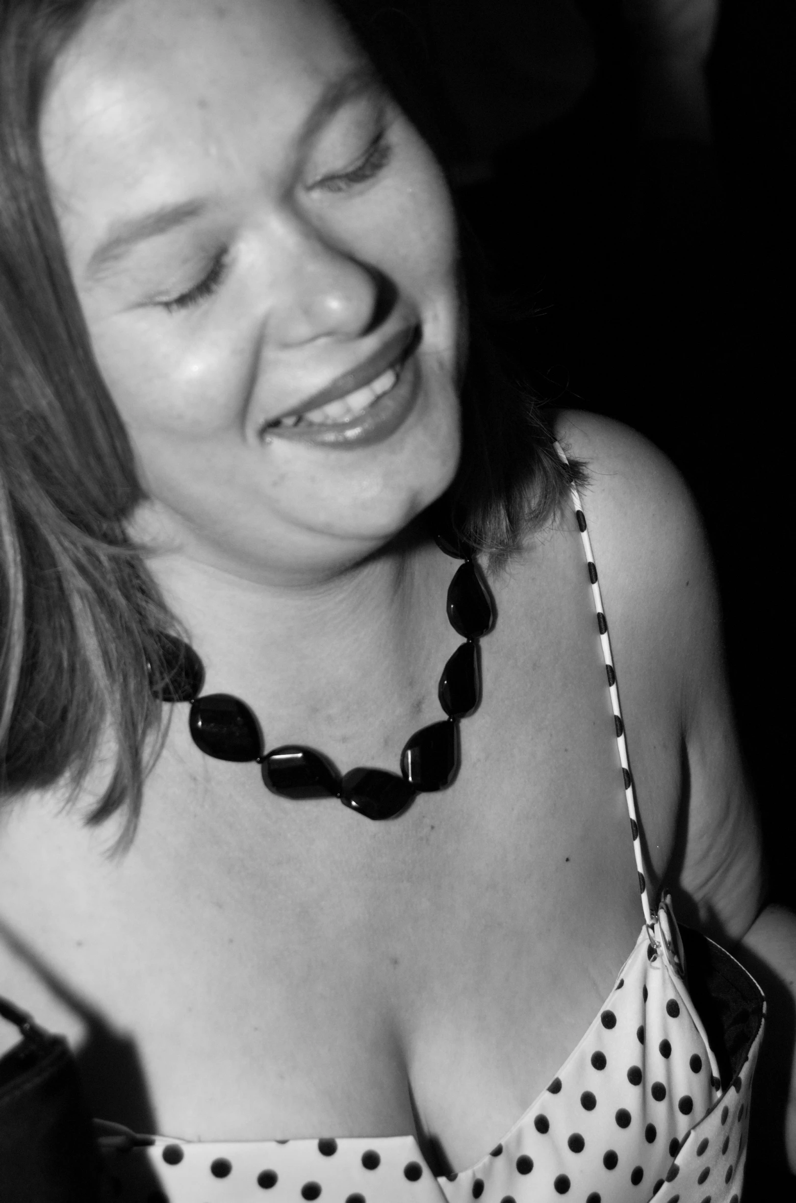 woman in dotted top laughing while wearing a large black necklace