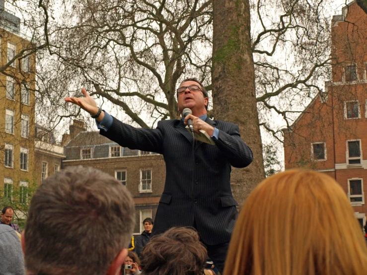 man speaking in a crowded town square with trees