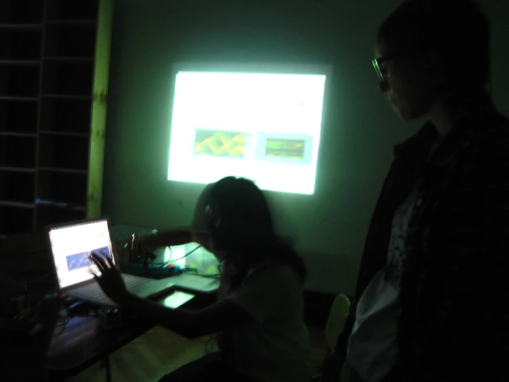 two people standing in front of a laptop in a dark room