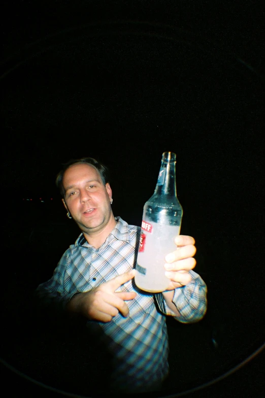 man standing at night holding a bottle of beer