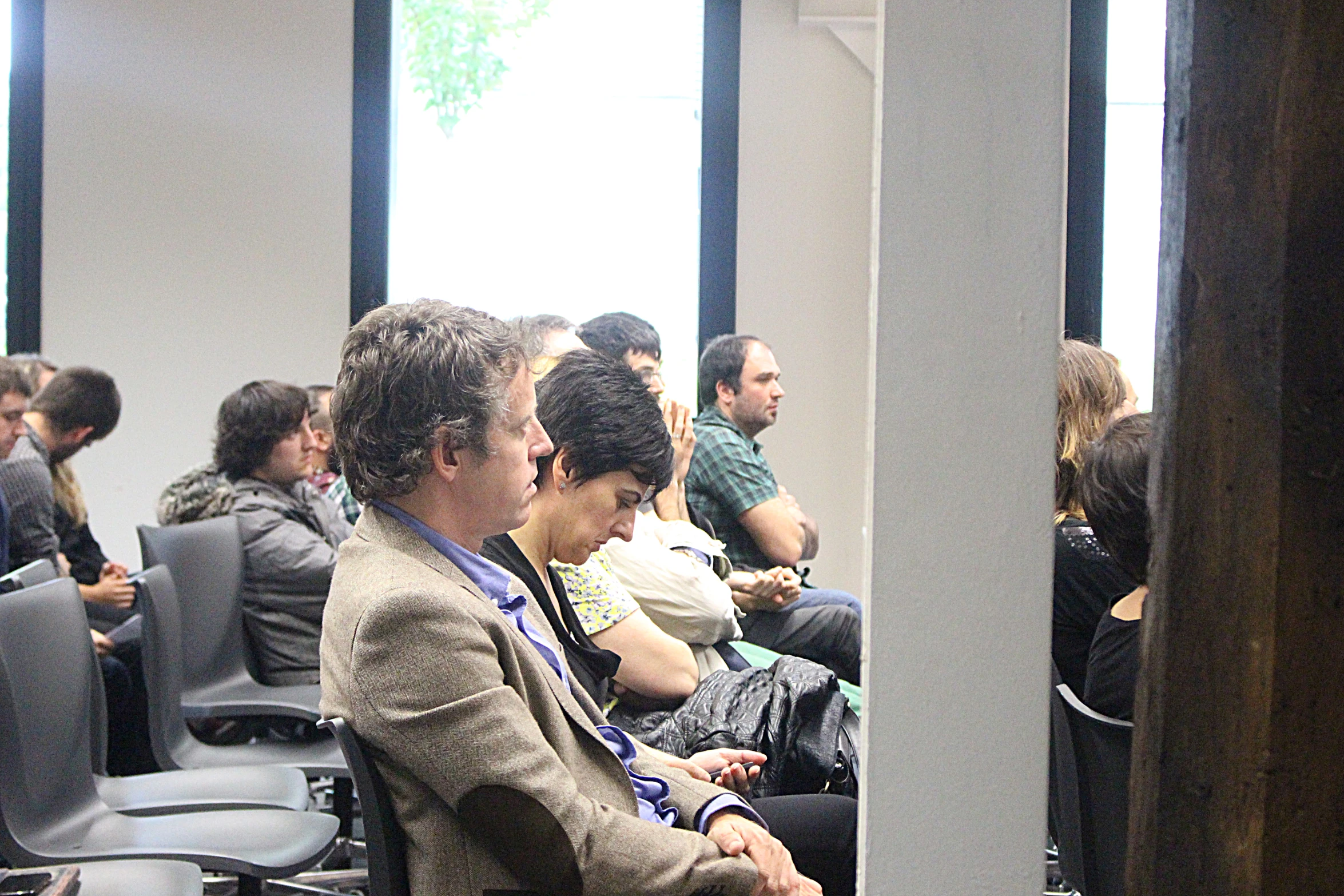 a group of people sit in chairs, watching a presentation