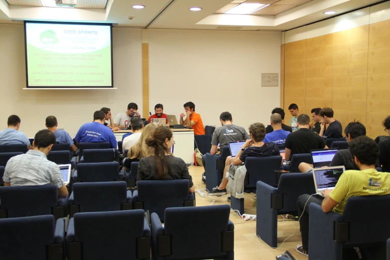 group of people sitting on blue chairs in front of large screen