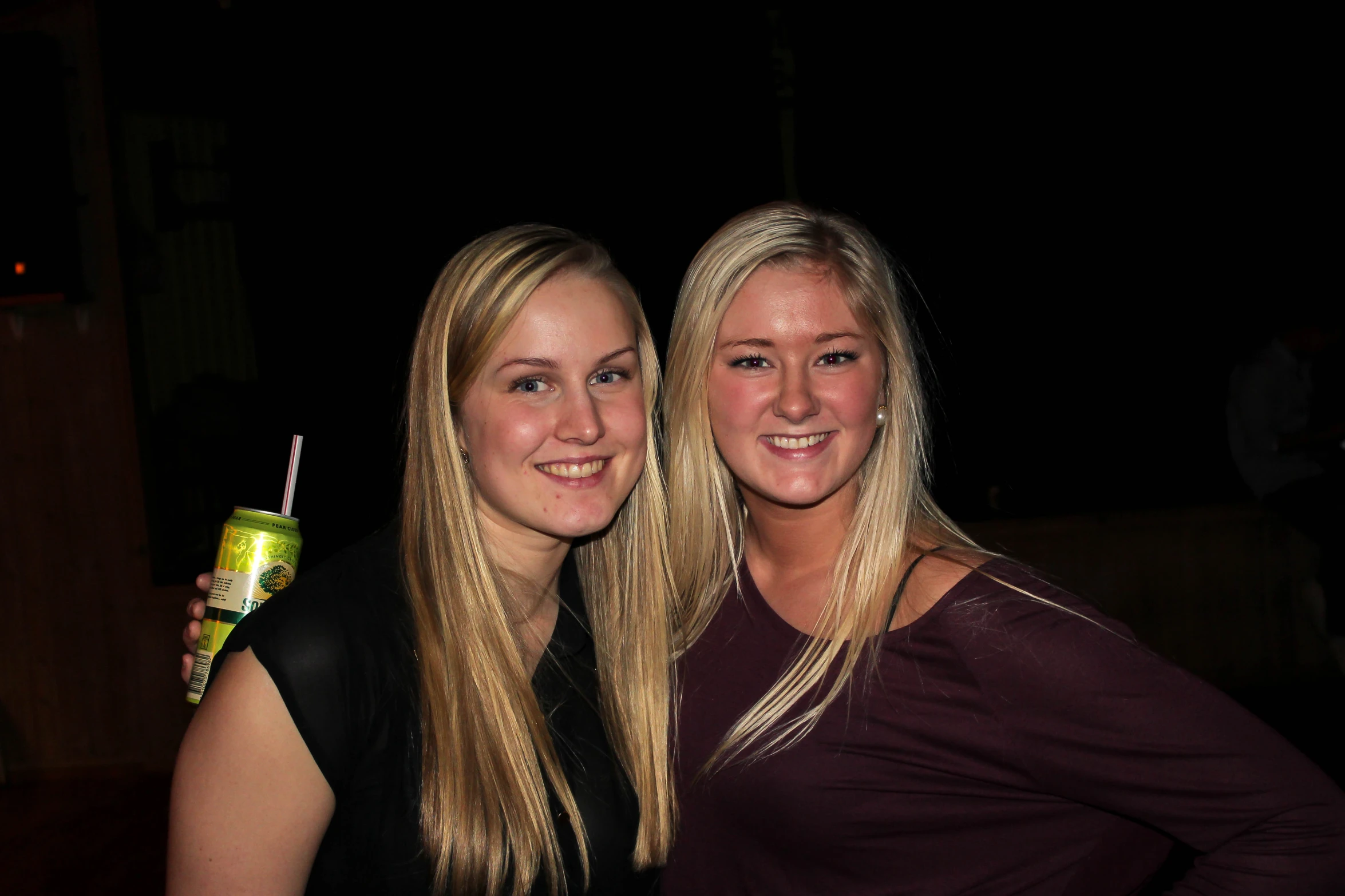 two women posing together holding beverages at a party