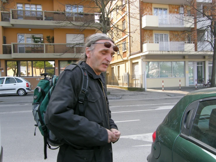 a man with glasses and a black jacket near a parked car