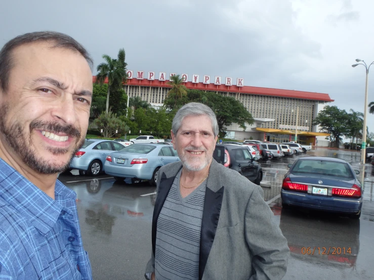 two men standing next to each other in front of a car parking lot