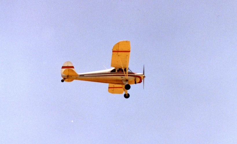 an older yellow biplane flying through a blue sky