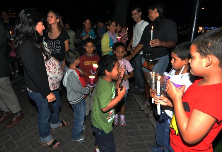 a little boy holding two small candles in front of a crowd