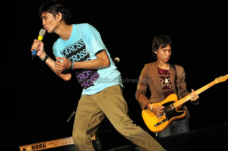 two boys playing guitar and singing on stage