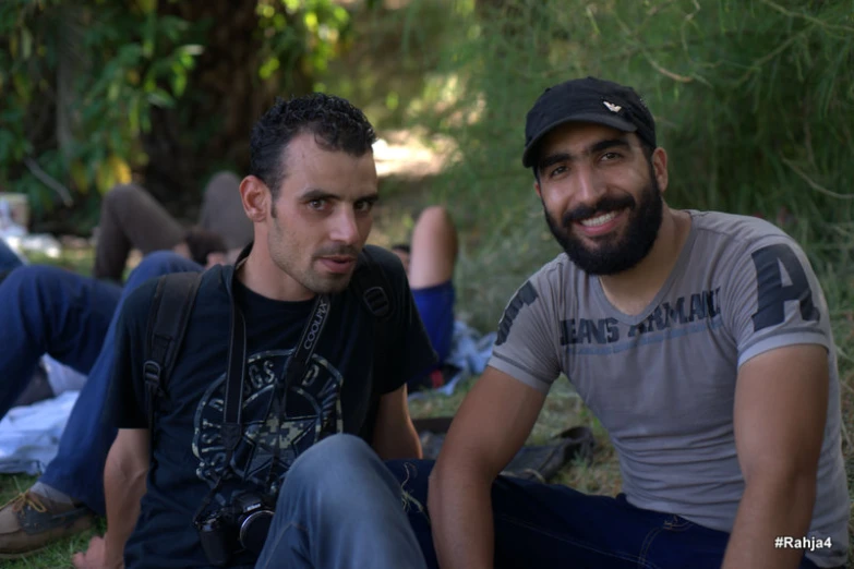 two men sitting on the ground in front of trees