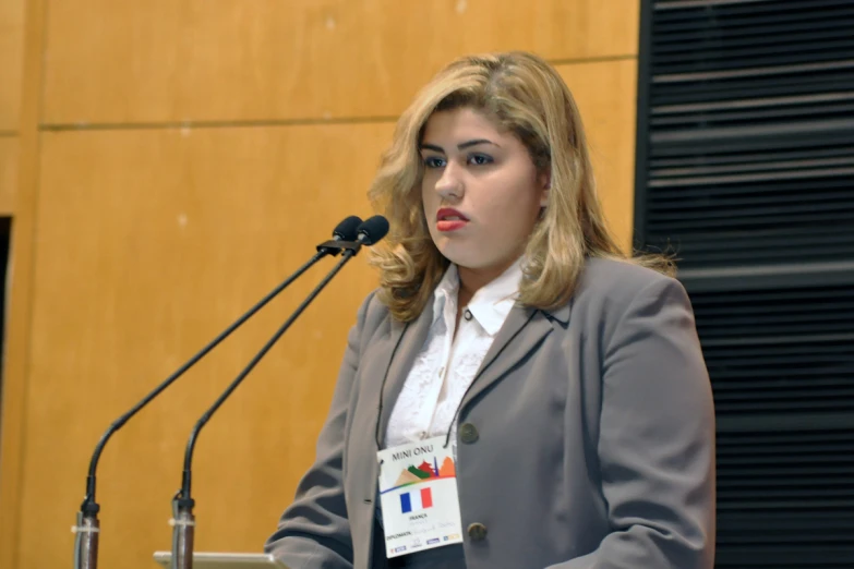 a woman speaking into microphone with two hands in front of her