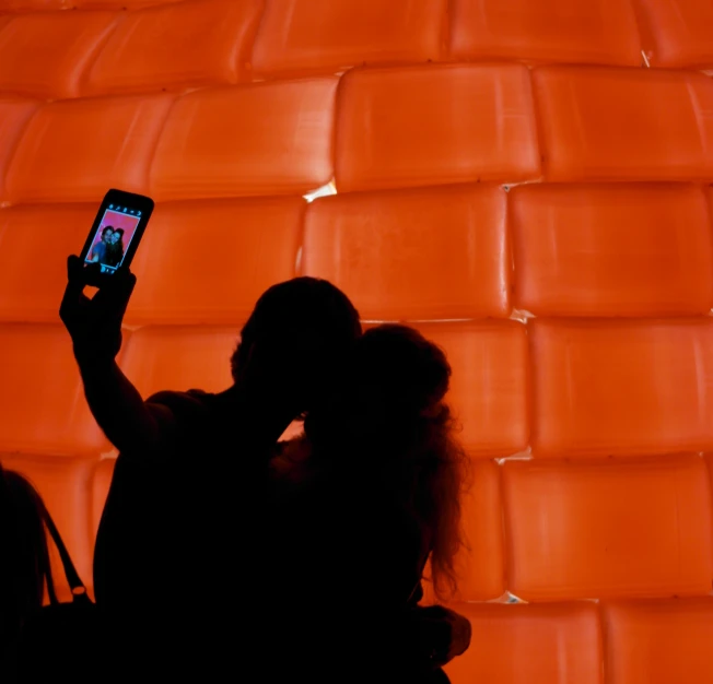 the shadow of a woman holding a cell phone is against an orange wall