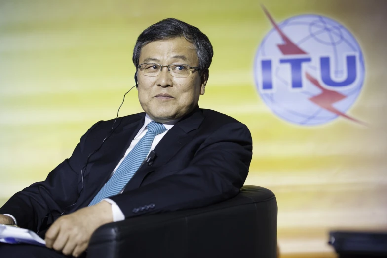 a man in suit and tie sitting next to a white sign