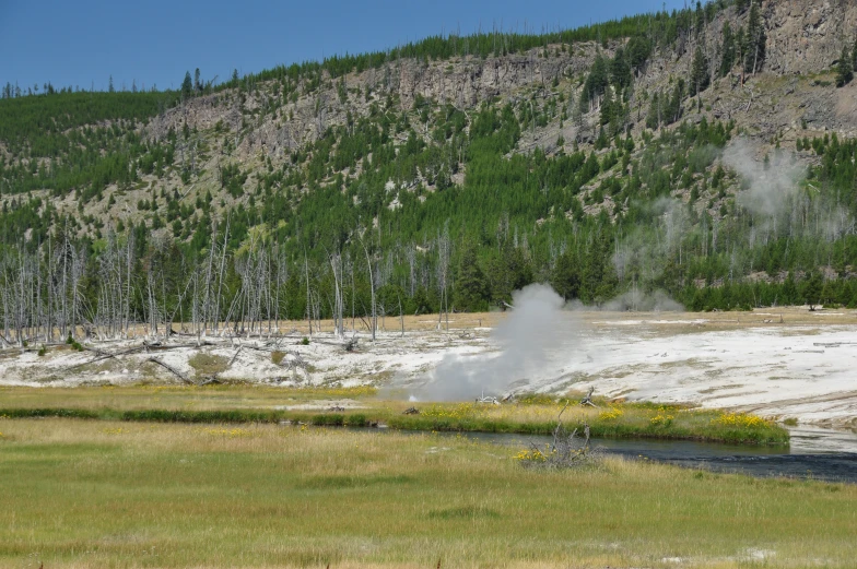 a steam machine near a river with mountains in the background