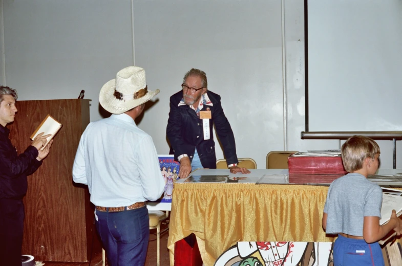 men wearing suits and hats stand by a table