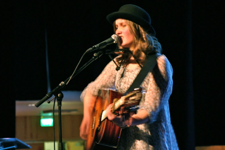 a woman holding a guitar while standing in front of a microphone