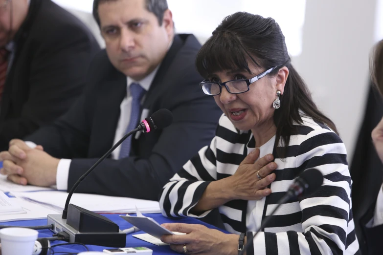 a woman sitting at a table talking into a microphone