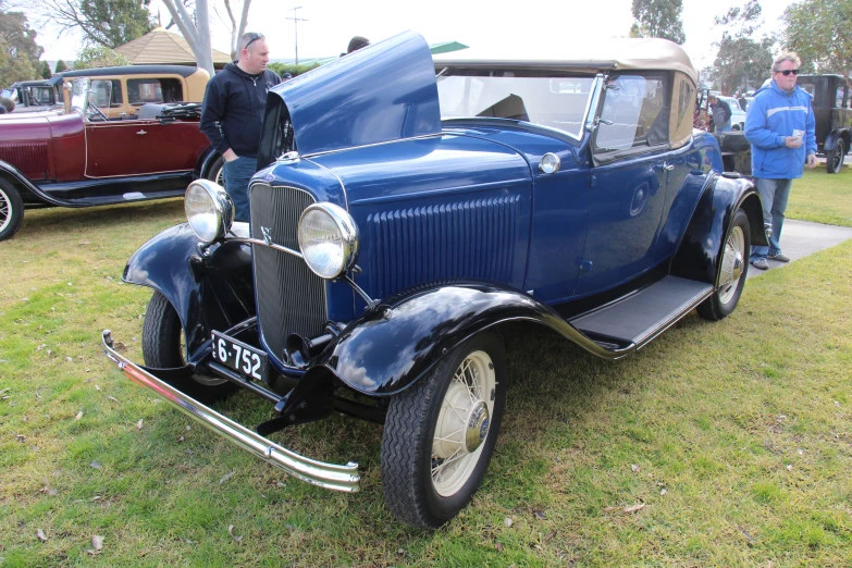 an older model car parked on a grass covered lot with other old fashioned cars in the background