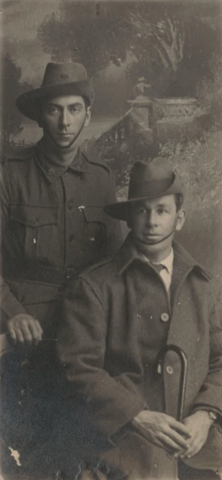 a man with a hat on sitting in front of another man wearing a trench coat