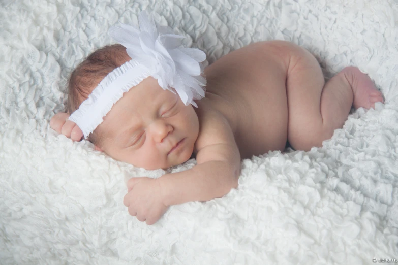a baby with a headband laying on top of a white blanket
