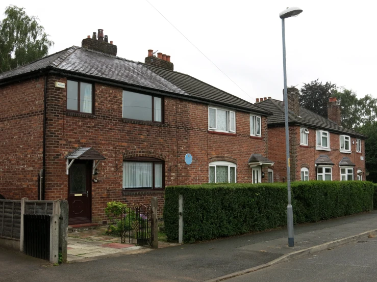 a brick two story home with hedges and shrubbery