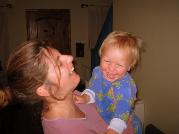 a smiling woman holds a toddler while he smiles