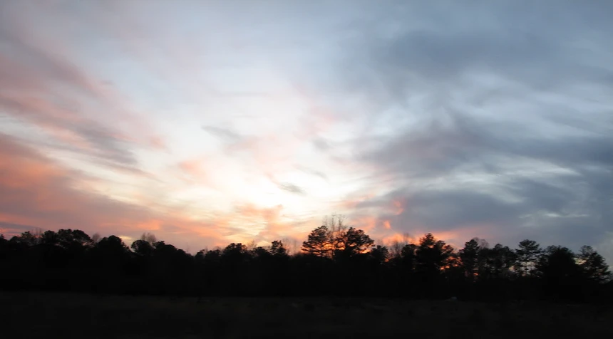 a sunset view of some trees and clouds in the distance