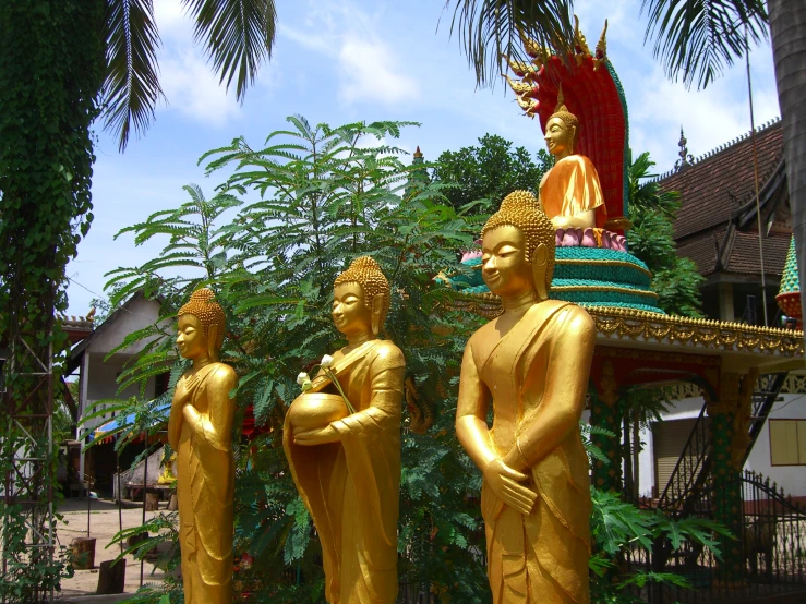 three gilded statues sitting next to each other in front of trees