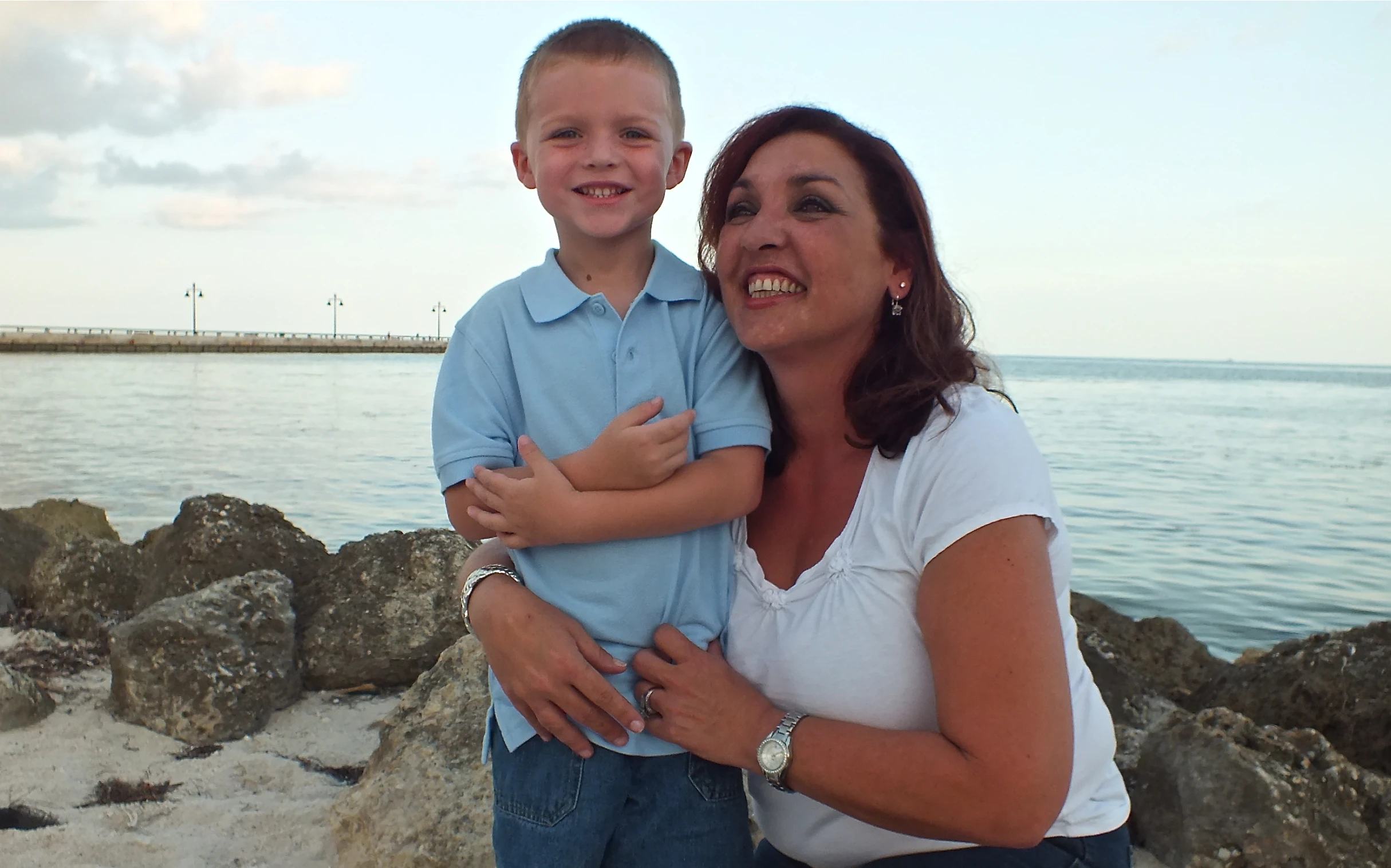 a woman holding a boy near water with rocky shoreline