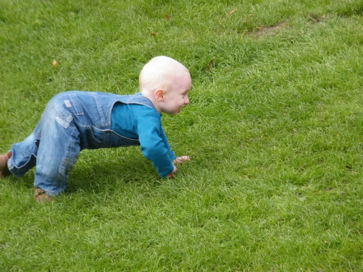 a baby standing in the grass and leaning forward