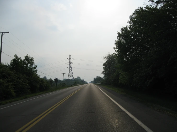 the view of a road with some telephone wires on one side and trees on the other