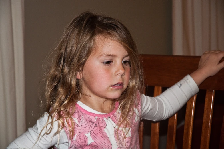 a girl in a pink and white shirt sitting at a table with a chair