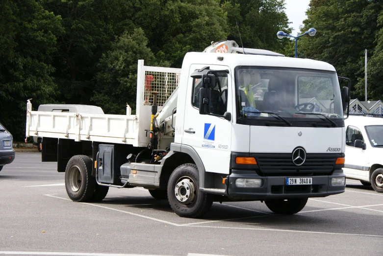 a white truck driving down a parking lot filled with lots of green trees