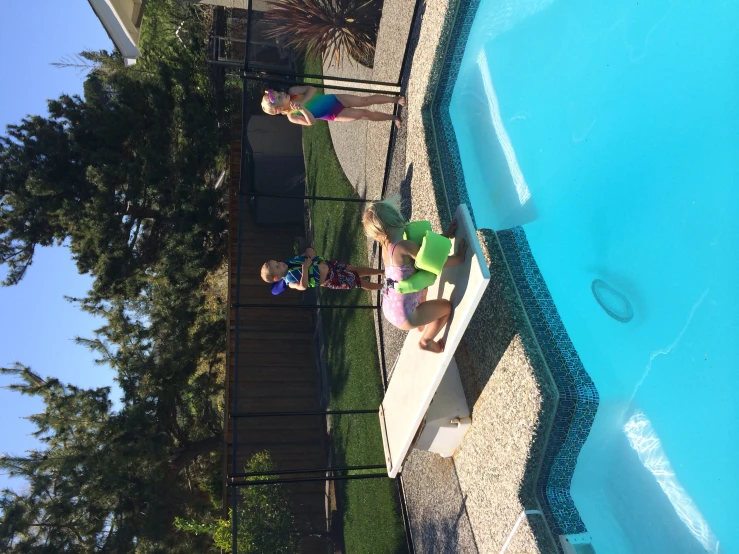 three children play on two floaties beside a swimming pool