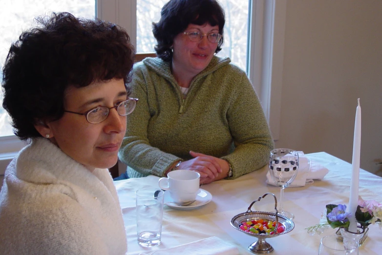 two women sitting at a table with some flowers and candles