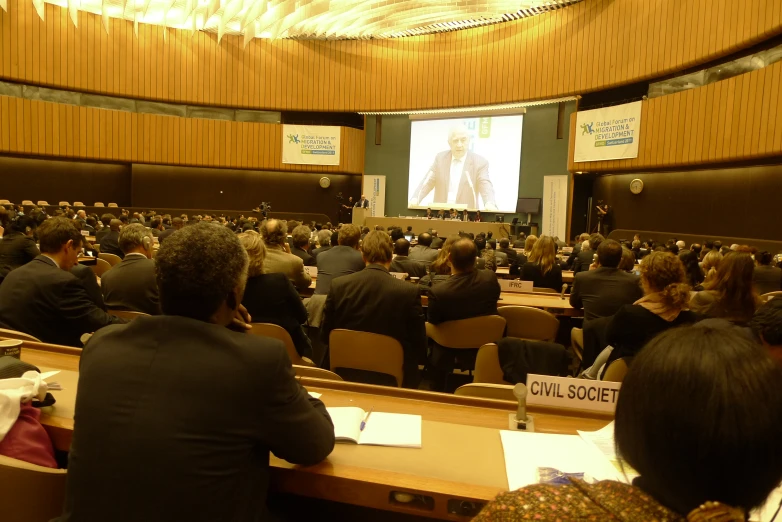 a group of people sitting around a table in front of a large screen