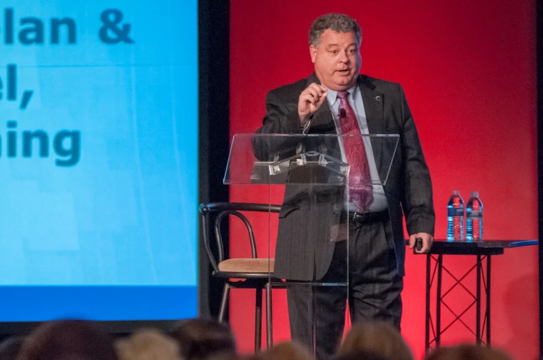 a man in a business suit is speaking at a podium