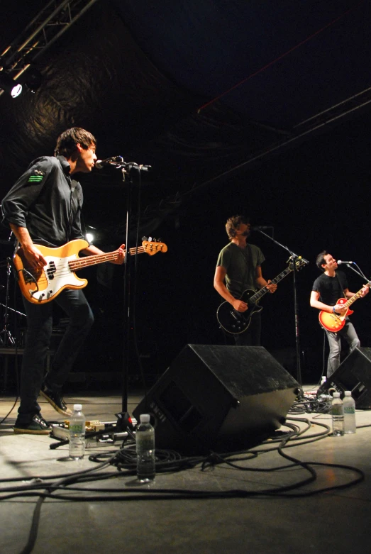 two men playing guitar while another man sings in front of a microphone