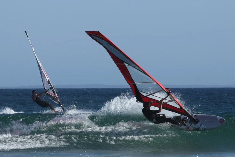 a man riding a sailboat next to a wind surfer