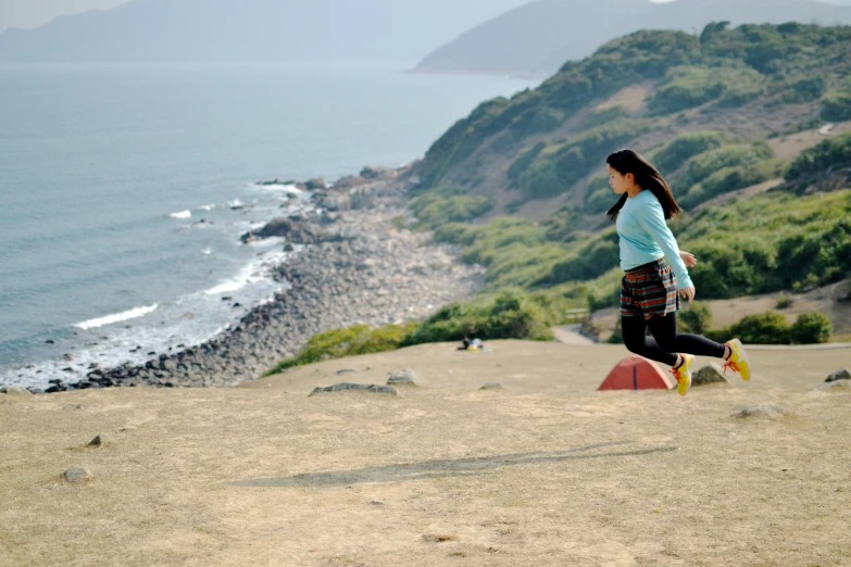 a woman with long hair walking on a cliff by the ocean