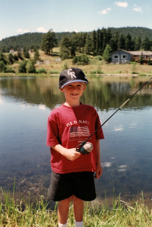 a boy in a red shirt and hat is fishing with a pole