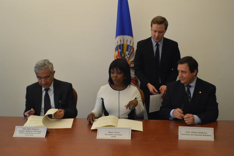 two black people sitting at a wooden desk in front of a microphone and two others are wearing business suits